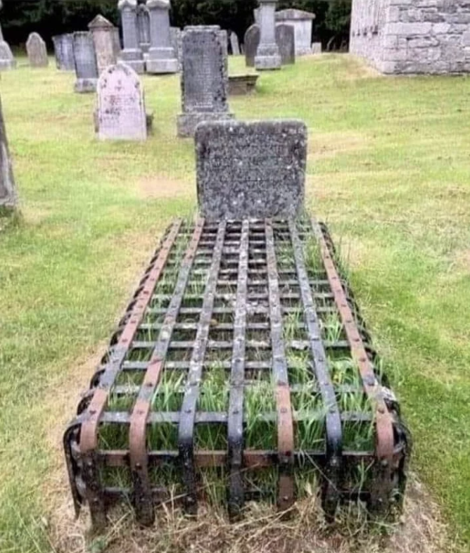 Iron grave cage on grassy surface with headstones and church in background