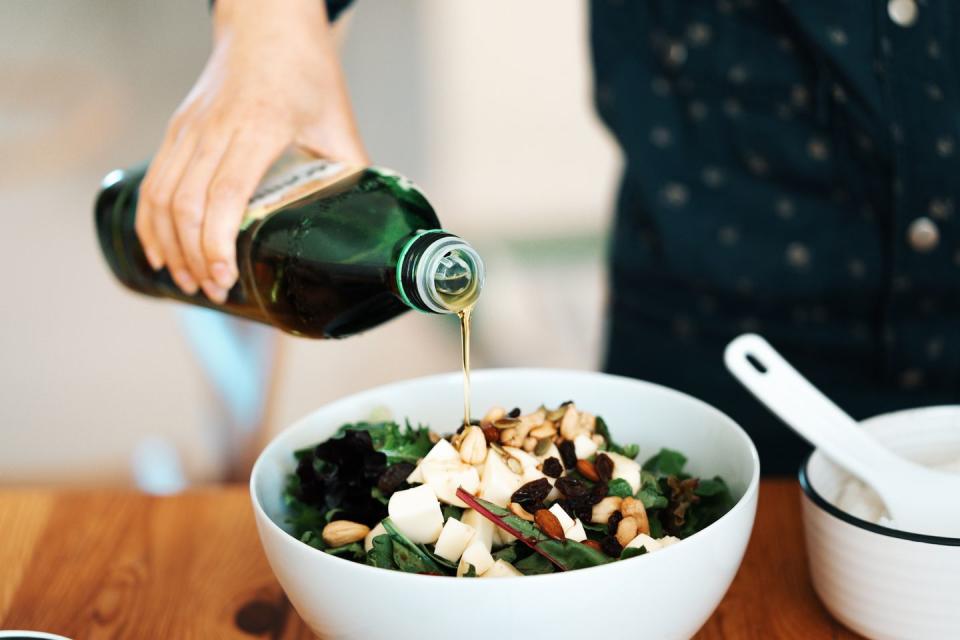 close up view of a bowl of fresh green salad with mozzarella, mixed nuts and dry fruits a woman’s hand was pouring olive oil into the salad