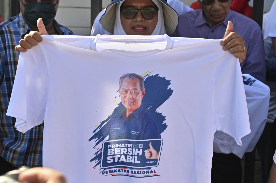 A supporter of former Prime Minister Muhyiddin Yassin shows a T shirt with his picture outside the Anti-Corruption Commission headquarters in Putrajaya, Malaysia, Thursday, March 9, 2023. Muhyiddin arrived Thursday at the anti-graft agency office for a second time in a month over alleged corruption in the award of government projects under his rule. (AP Photo)
