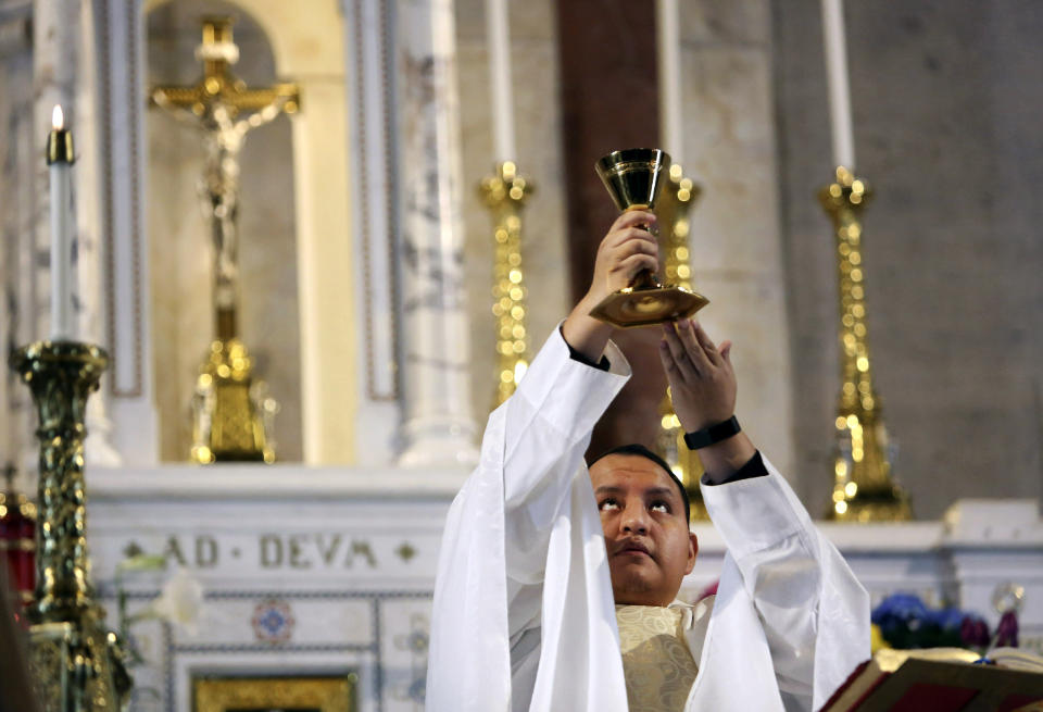 In this April 19, 2020, photo, the Rev. Joseph Dutan, 32, lifts the chalice during Sunday Mass at an empty St. Brigid Church in the Brooklyn borough of New York. Dutan recalls how he lifted the chalice in the empty church and felt a flood of emotions: grief, the pain of isolation, even doubt. But also, the promise of hope that is the gift of every Easter -- even in the midst of a pandemic that had already robbed him and his community of so much, and threatened to take so much more. (AP Photo/Jessie Wardarski)