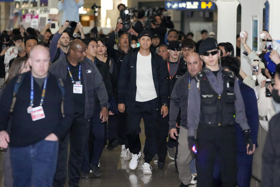 CORRECTS DATE - Los Angeles Dodgers' Shohei Ohtani, center, walks with an entourage during the baseball team's arrival at Incheon International Airport, Friday, March 15, 2024, in Incheon, South Korea, ahead of the team's baseball series against the San Diego Padres. (AP Photo/Lee Jin-man)