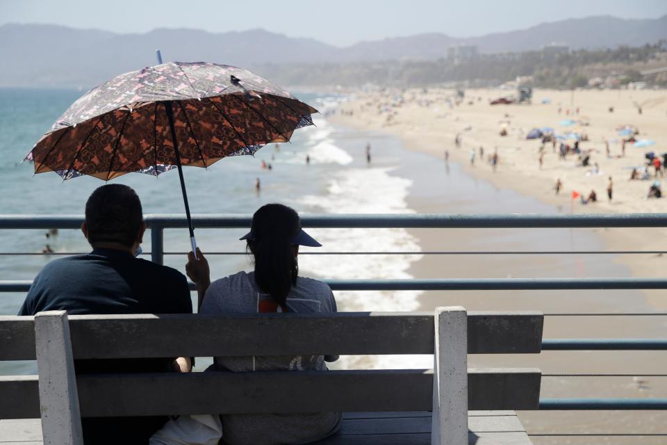 Visitors sit on a bench on the pier amid the coronavirus pandemic Sunday, July 12, 2020, in Santa Monica, California. The Hampton Beach Area Commission is undertaking a study to judge the feasibility and impact of building a pier off Hampton Beach, N.H.