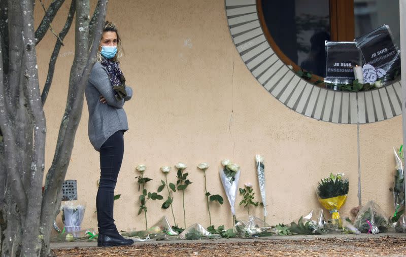 A woman stands next to flowers at the Bois d'Aulne college after the attack in the Paris suburb of Conflans St Honorine