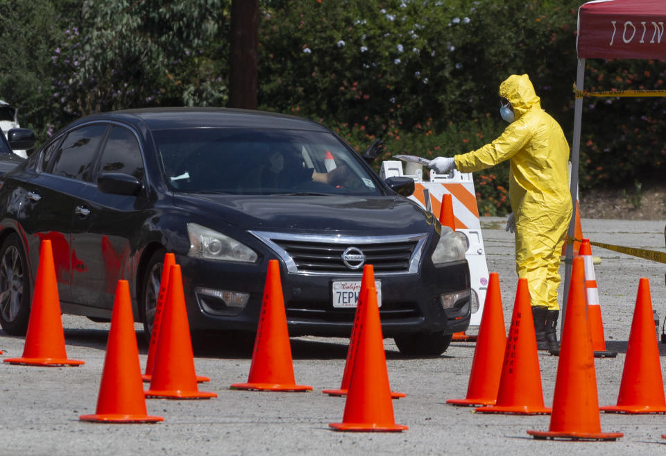 Los Angeles Fire Department officials deliver testing kits to a waiting motorists at a COVID-19 drive-up testing site in Elysian Park, Thursday, April 2, 2020. Officials say hand-washing and keeping a safe social distance are priorities in battling the COVID-19 virus. (AP Photo/Damian Dovarganes)