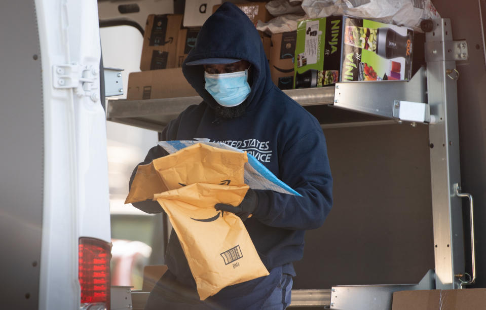 A mailman wearing a mask and gloves to protect himself and others from COVID-19, known as coronavirus, loads a postal truck with packages at a United States Postal Service (USPS) post office location in Washington, DC, April 16, 2020. - For many Americans, checking the mailbox is a daily ritual, a constant in a quickly changing world that can yield anything from wedding invitations to tax audits to new clothes. But as with many ordinary things as the coronavirus crisis unfolds, the US Postal Service -- already compromised by a mountain of debt -- has a most uncertain future. (Photo by SAUL LOEB / AFP) (Photo by SAUL LOEB/AFP via Getty Images)