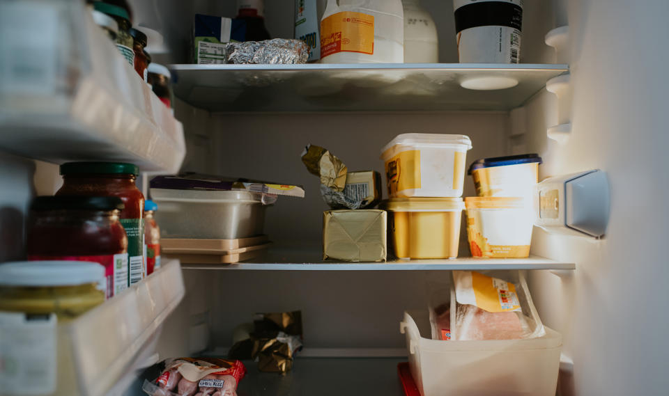 An open refrigerator with various food items including containers, jars, and wrapped packages on multiple shelves. No people are present