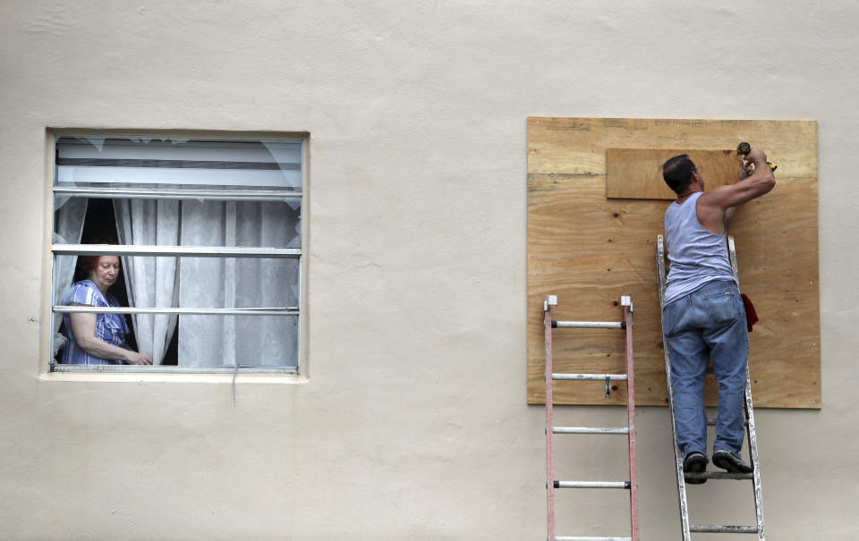 A King Point resident looks through her broken window as a man boards up another broken window from an apparent overnight tornado spawned from Hurricane Ian at Kings Point 55+ community in Delray Beach, Fla., on Wednesday, Sept. 28, 2022. (Carline Jean /South Florida Sun-Sentinel via AP)