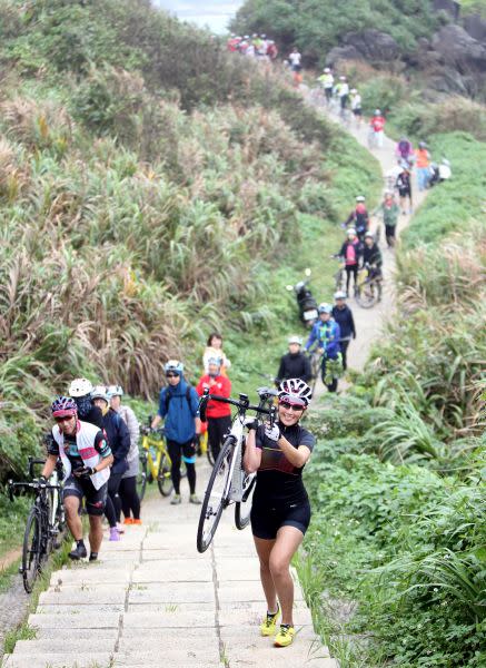 為了親近富貴角燈塔，燈塔極點慢旅代言人邱念慈(前)和車友們一起扛車前進。中華民國自行車騎士協會／提供。