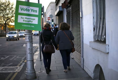 Woman holding hands walk past a Yes vote campaign poster in central Dublin as Ireland holds a referendum on gay marriage, May 22, 2015. REUTERS/Darren Staples