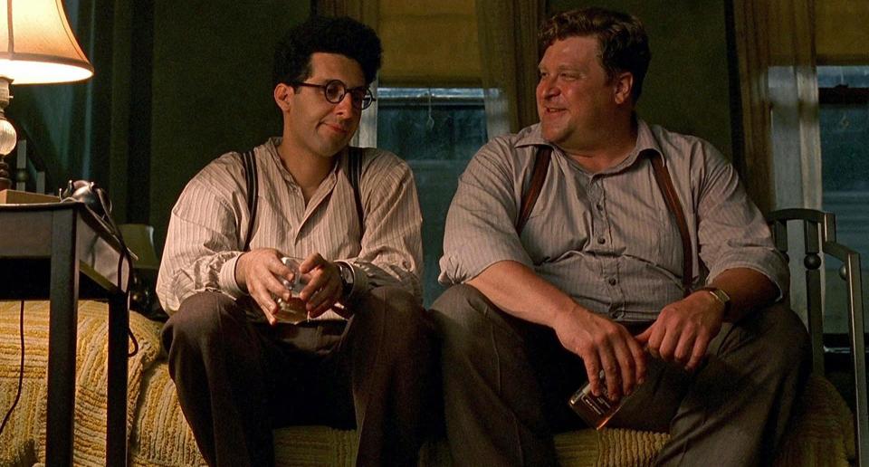 John Turturro and John Goodman sitting on a bed