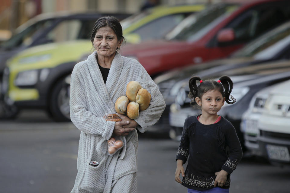 FILE- In this Sunday, Oct. 27, 2019 file picture a woman clutching loafs of bread and some eggs walks along with a child by a cleaning facility during a visit to a poor area of the Romanian capital by Romanian caretaker Prime Minister and presidential candidate supported by the ruling Social Democratic party (PSD) Viorica Dancila in Bucharest, Romania. Romania will hold presidential elections on Nov. 10. (AP Photo/Vadim Ghirda, File)