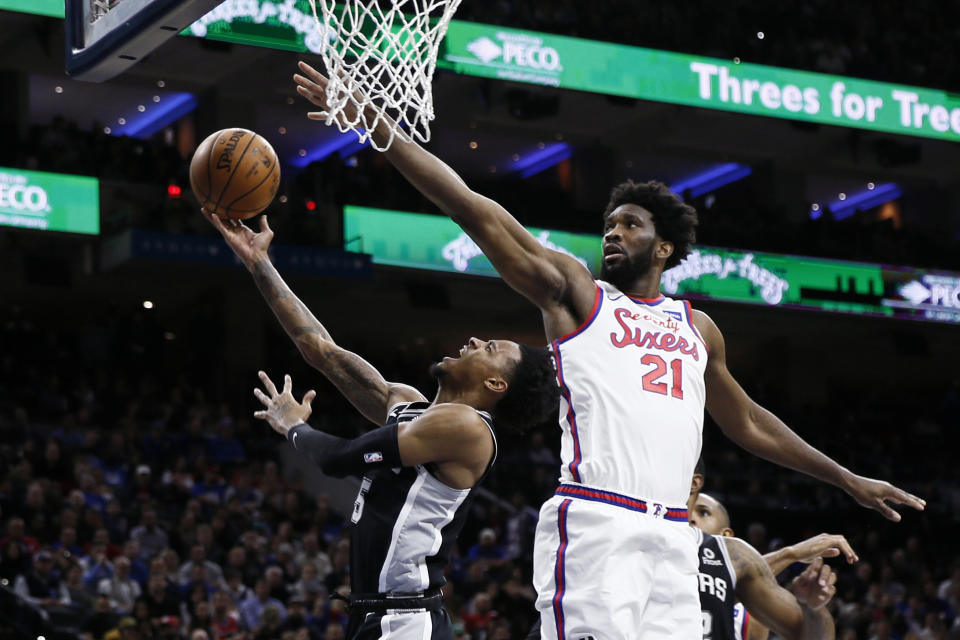 San Antonio Spurs' Dejounte Murray, left, releases a shot next to Philadelphia 76ers' Joel Embiid during the second half of an NBA basketball game Friday, Nov. 22, 2019, in Philadelphia. Philadelphia won 115-104. (AP Photo/Matt Slocum)