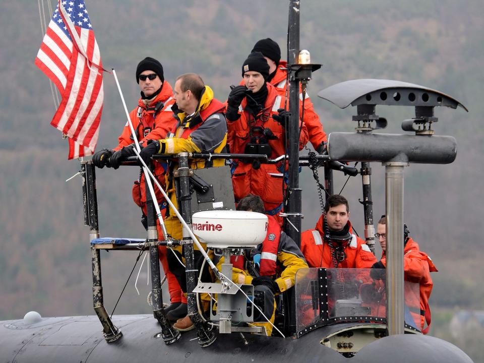 Navy sailors stand on sail of Virginia-class attack submarine USS Virginia surrounded by an American flag and periscope equipment