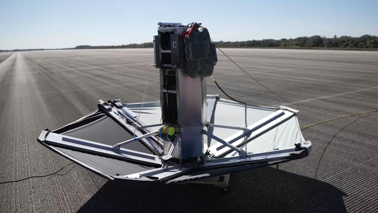  A device that resembles a large upside-down umbrella sits on a black asphalt runway. 