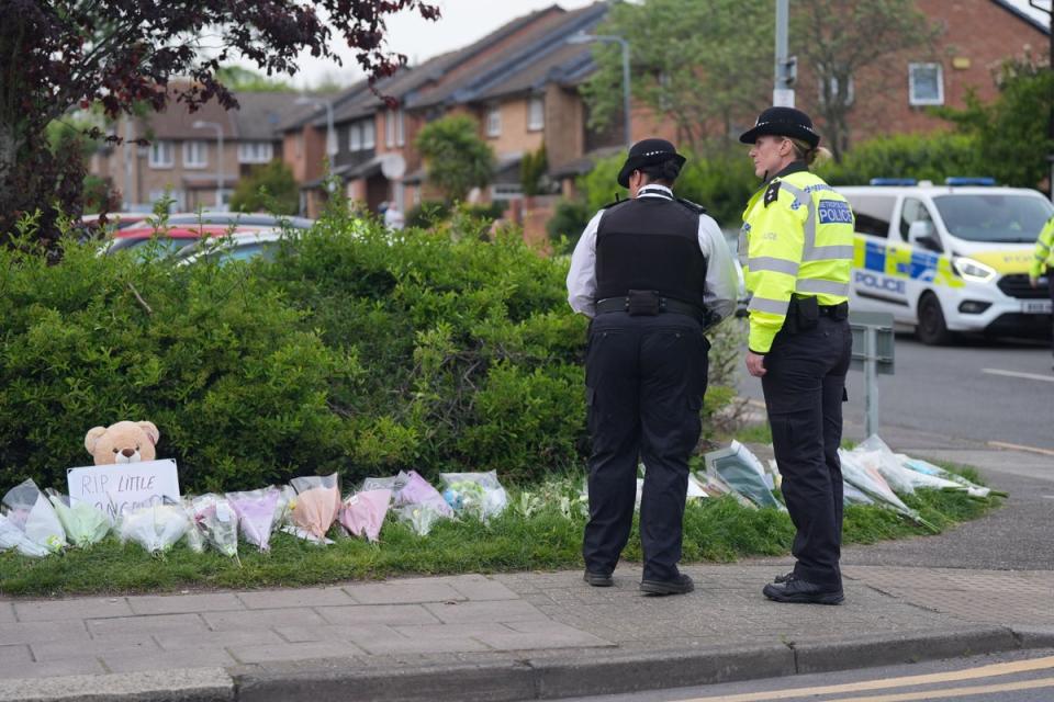 Police officers look at flowers laid at the scene of the incident in Hainault where 14-year-old Daniel Anjorin was killed on Tuesday (PA Wire)