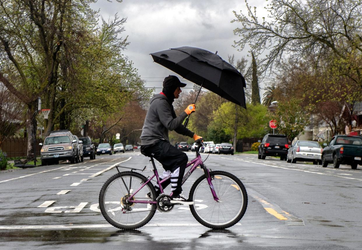 A cyclist shields himself from the rain with an umbrella as he rides down Fremont Street at Baker Street in Stockton on Tuesday, Mar. 21. 2023.