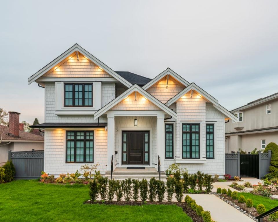 A modern, white, well-lit farmstyle house is shown. A grassy yard lines a walkway leading up to the front door.