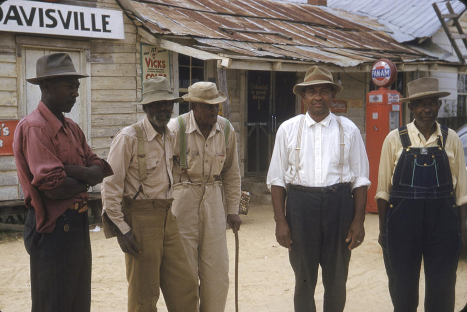 Group of five men in vintage workwear standing in front of a rustic wooden building