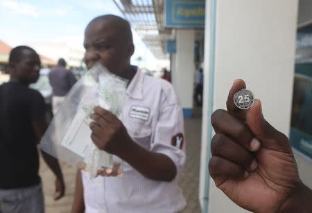 A man shows a new Zimbabwean 25 cents coin in front of a bank in Harare, December 18, 2014. REUTERS/Philimon Bulawayo