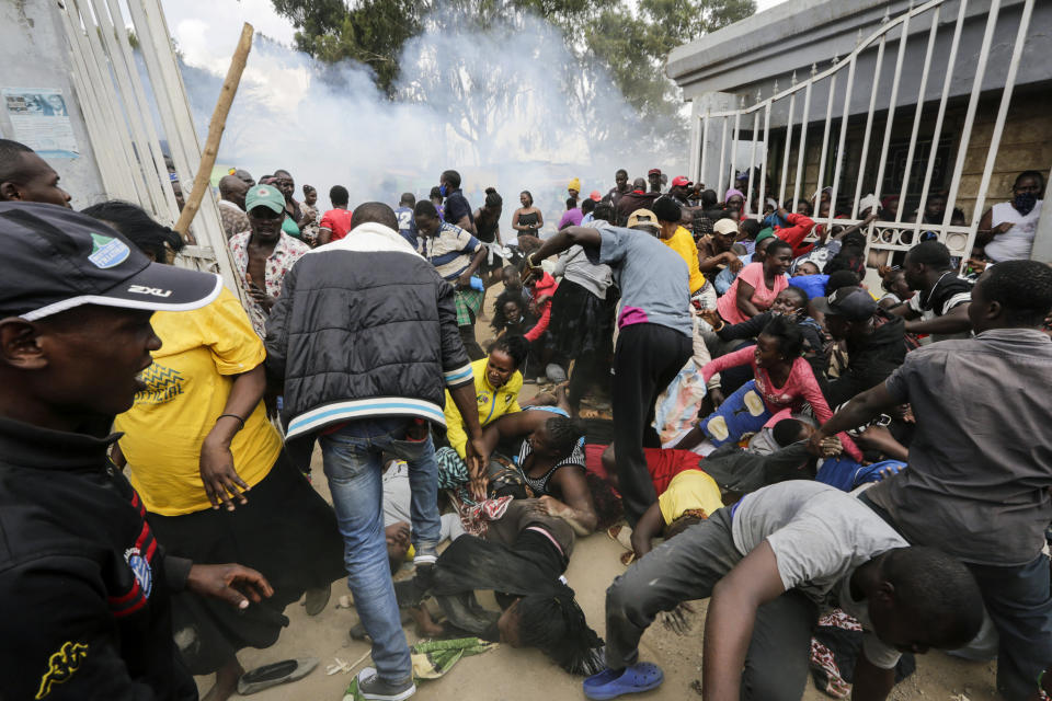 Residents desperate for a planned distribution of food for those suffering under Kenya's coronavirus-related movement restrictions push through a gate and create a stampede, causing police to fire tear gas and leaving several injured, at a district office in the Kibera slum, or informal settlement, of Nairobi, Friday, April 10, 2020. (AP Photo/Khalil Senosi)