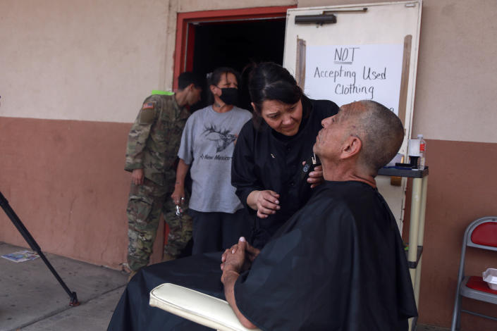 Wildfire evacuee Domingo Martinez gets a haircut from Jessica Aragón outside an emergency shelter in Las Vegas, N.M., on Saturday, May 7, 2022. Martinez left his home in a wooded rural area northwest of Las Vegas and stayed in a safer neighborhood with his son. The people lined up behind him are meeting with federal officials for help with assistance claims. (AP Photo/Cedar Attanasio)