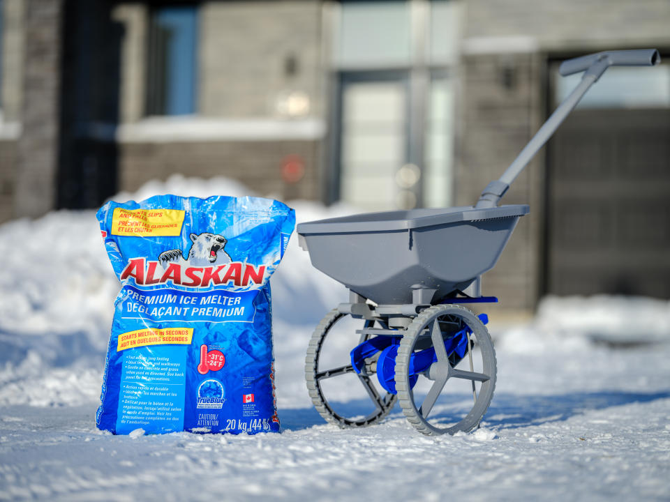 A bag of Canadian Tire Alaskan Premium Ice Melt and an ice melt spreader on a snow covered driveway