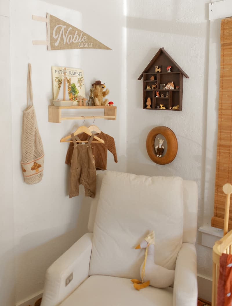 corner of white nursery with white armchair and warm colored art and decor