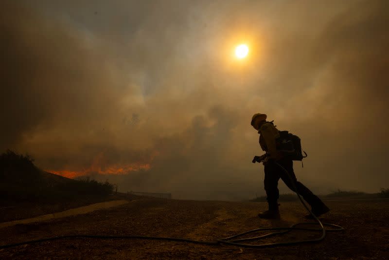 A firefighter uses a homeowners garden hose to help battle the Silverado Fire, a wind driven wildfire near Irvine, California