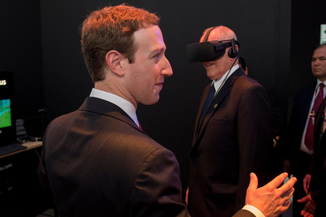 Mark Zuckerberg standing near a man wearing a black virtual-reality headset.