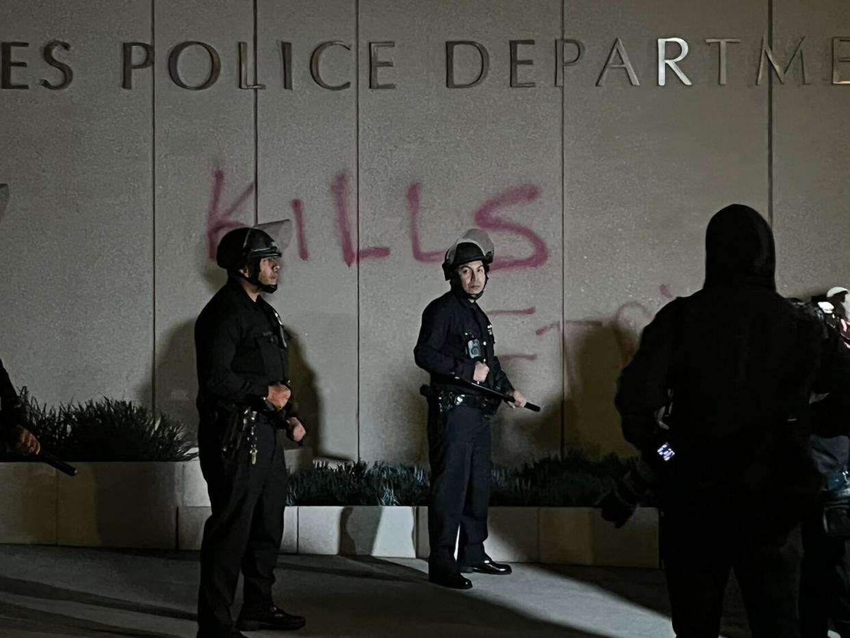 Police officers in front of the word "kills" spray painted underneath the "Los Angeles Police Department" sign