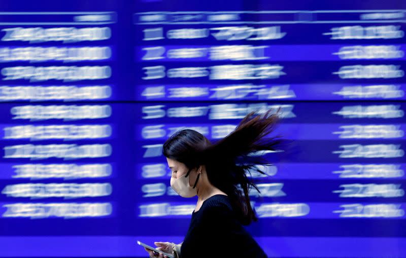 FILE PHOTO: A passerby walks past an electric monitor displaying recent movements of various stock prices outside a bank in Tokyo