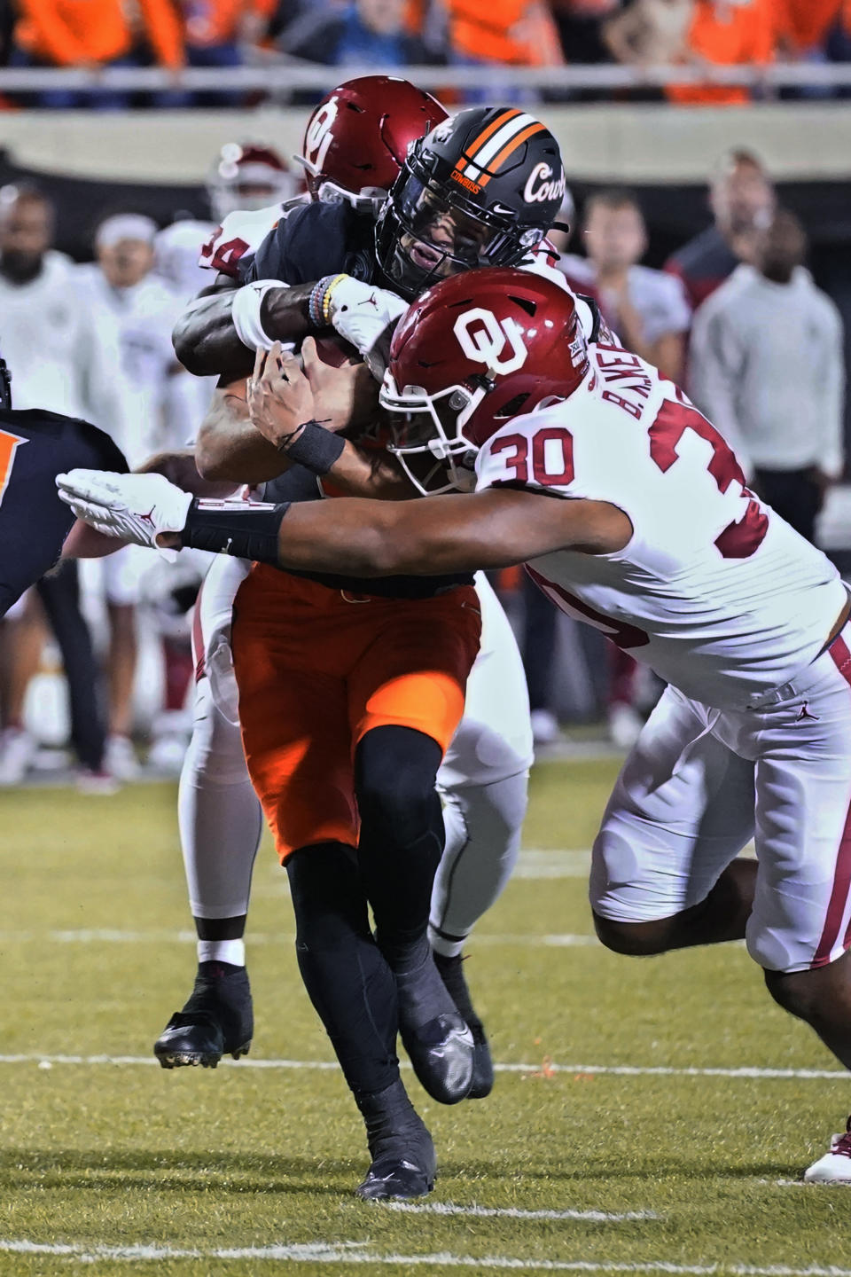 Oklahoma State quarterback Spencer Sanders, center, is tackled by Oklahoma linebackers Brian Asamoah, left, and Brynden Walker (30) during the first half of an NCAA college football game Saturday, Nov. 27, 2021, in Stillwater, Okla. (AP Photo/Sue Ogrocki)