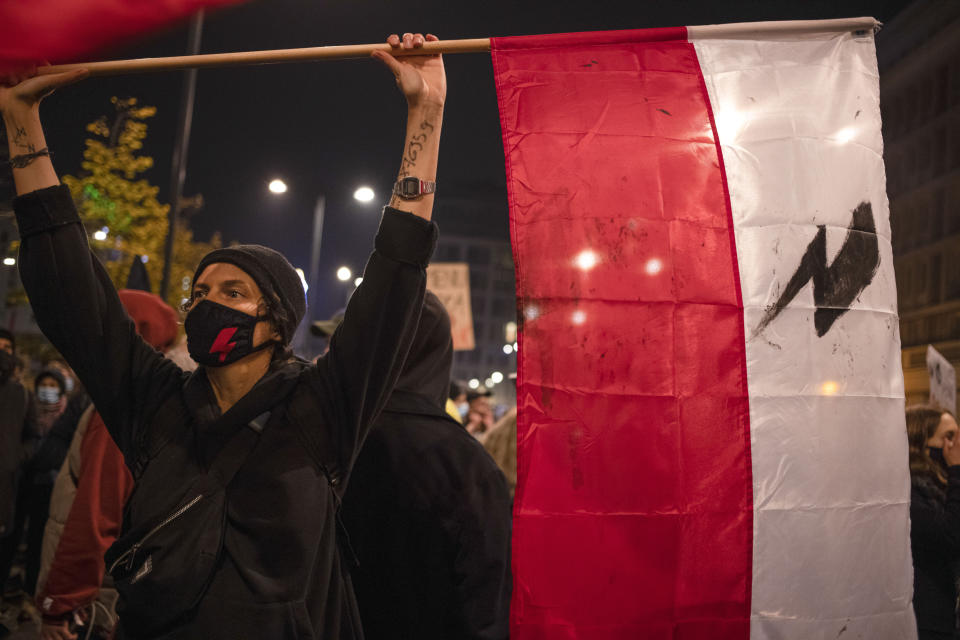 A demonstrator, with the phone number of a legal councilor written on their arm, holds the Polish flag during a protest against a top court ruling restricting abortions in Warsaw, Poland, Wednesday, Nov. 18, 2020. Poland already had one of Europe's most restrictive abortion laws, and the ruling would mean that the only legal reasons for abortion would be rape, incest or if the woman's life is in danger. (AP Photo/Agata Grzybowska)