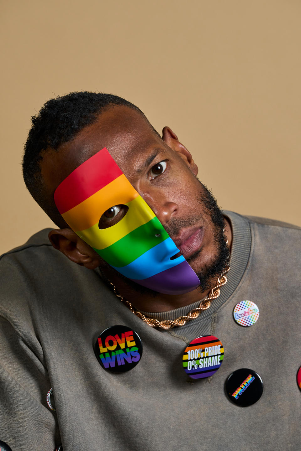Marlon Wayans wearing a rainbow mask and a gray sweatshirt adorned with LGBTQ+ supportive pins, including "Love Wins" and "100% Pride, 0% Shame."