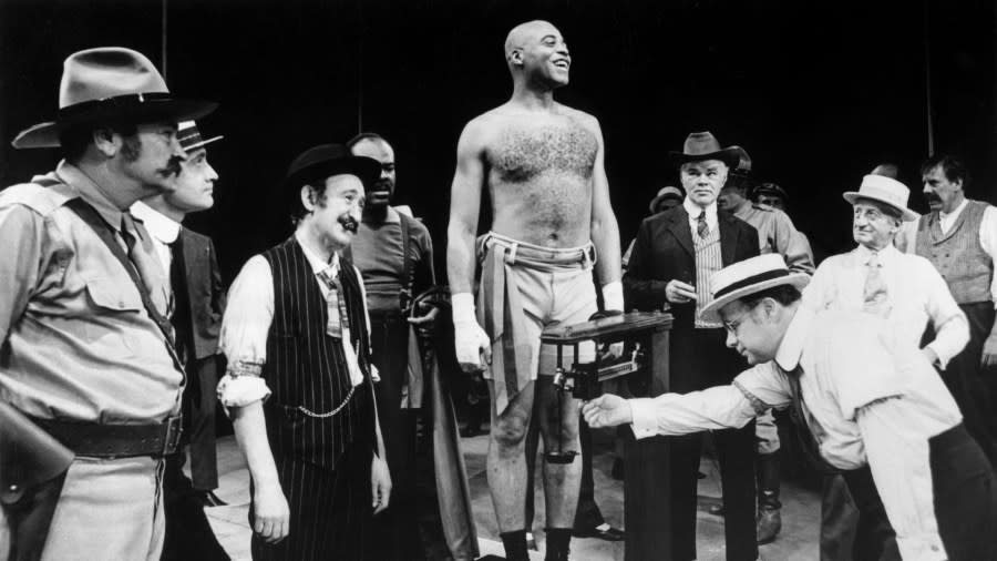 James Earl Jones, wearing athletic shorts and boxing shoes, stands proudly atop a scale during a weigh-in scene.