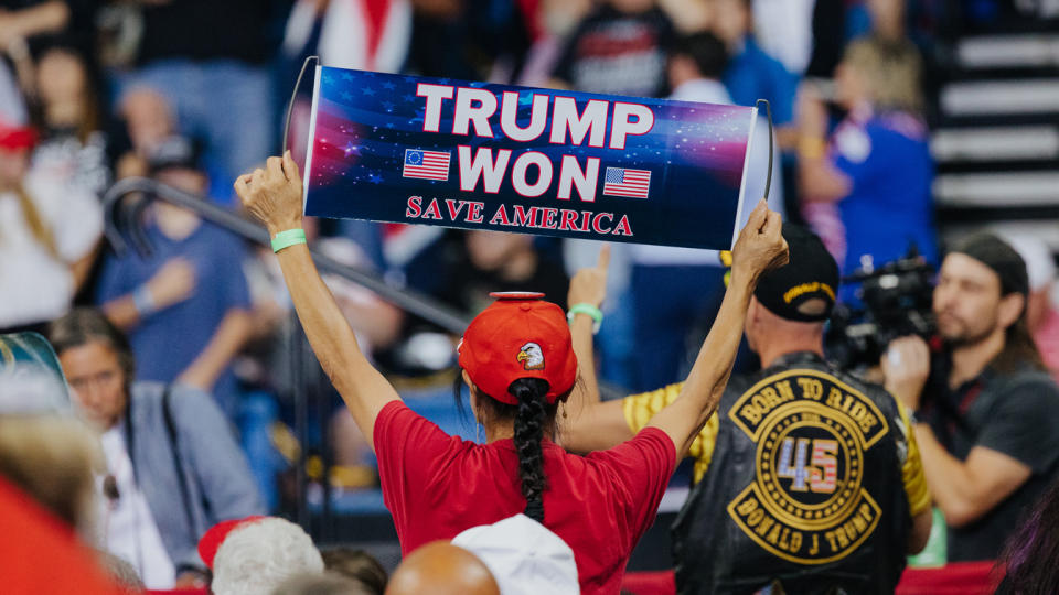 A rally attendee holds a banner reading: Trump Won, Save America. 