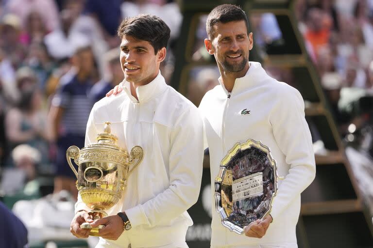 Carlos Alcaraz sostiene la copa de Wimbledon, mientras Novak Djokovic parece felicitarlo; el serbio llenó de elogios a su vencedor en la gran final en el All England