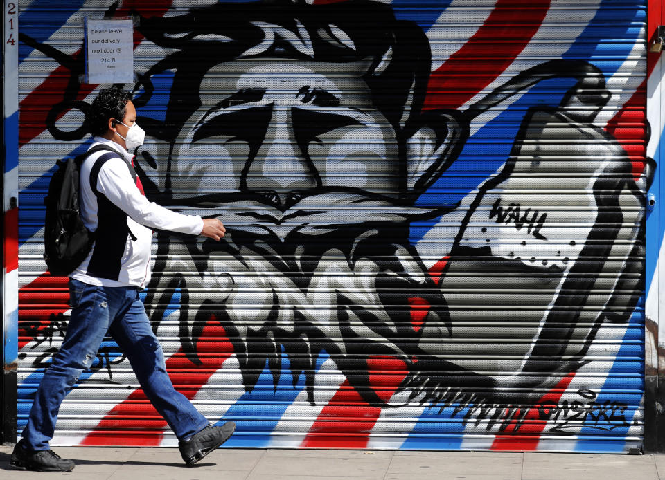 A man walks past graffiti sprayed shutters of a closed barber hair cutter shop in London, Tuesday, June 23, 2020. The closing of restaurants, hair cutters and pubs will be under review as the UK relax coronavirus lockdown measures implemented to stem the spread of the deadly virus.(AP Photo/Frank Augstein)