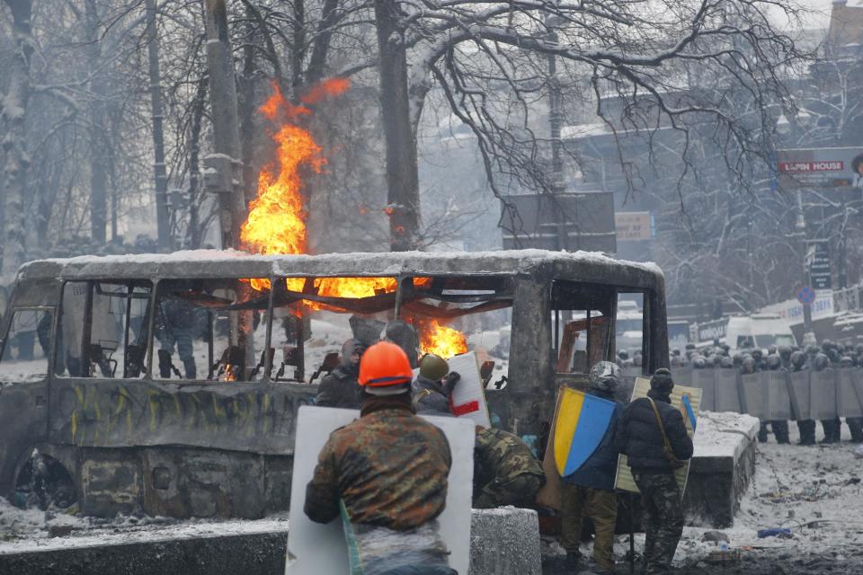 Protesters shield themselves behind a burned vehicle during clashes with police in central Kiev, Ukraine, early Wednesday, Jan. 22, 2014. Two people died in clashes between protesters and police in the Ukrainian capital Wednesday, according to medics on the site, a grim escalation of the country’s two-month-long political crisis. (AP Photo/Sergei Grits)