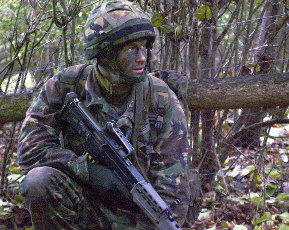 prince harry wearing camouflage and face paint and holding a gun during military training