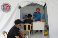 Health workers perform a rapid test on a man at a parking lot that has been converted into an extension of the Gat Andres Bonifacio Memorial Medical Center in Manila, Philippines on Monday, Aug. 3, 2020. Philippine President Rodrigo Duterte is reimposing a moderate lockdown in the capital and outlying provinces after medical groups appealed for the move as coronavirus infections surge alarmingly. (AP Photo/Aaron Favila)