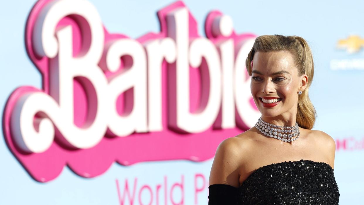 margot robbie smiling for a photo in front of the barbie movie logo