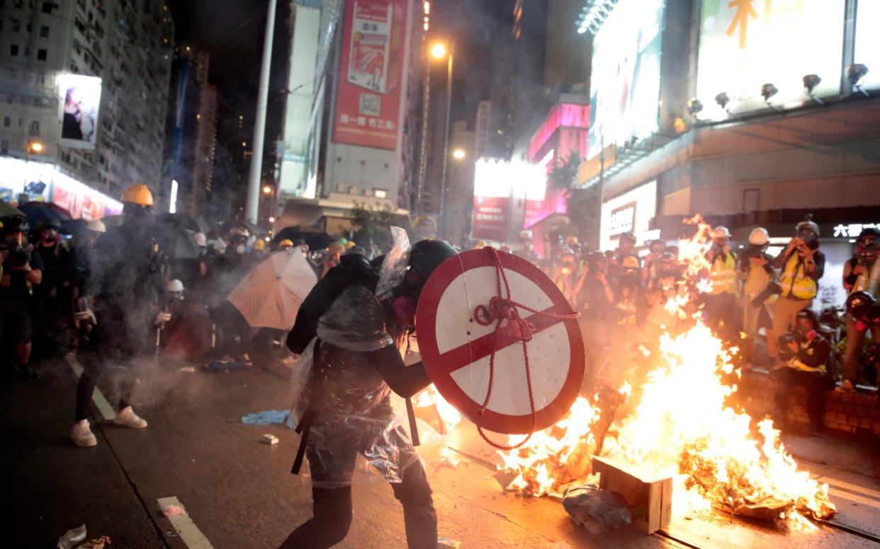 A protester uses a shield to cover himself as he faces police in Hong Kong - AP