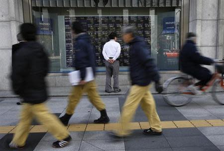 A man looks at a stock quotation board as passers-by walk past outside a brokerage in Tokyo January 28, 2014. REUTERS/Toru Hanai