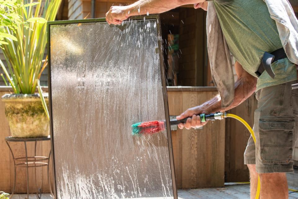 Man washing window screens with brush and water 