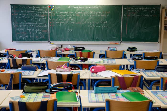 Classroom with empty desks and chairs, various school supplies on the desks, and French writing on the chalkboard