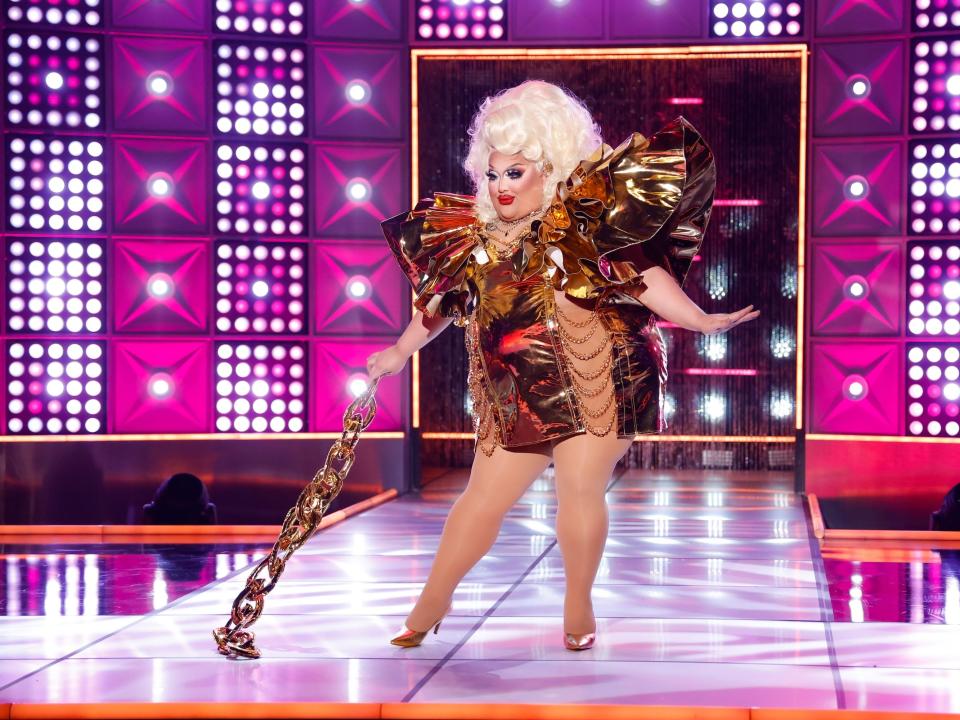Mistress Isabelle Brooks poses on the runway in a gold metallic dress with chain details, and a gold chain prop in this still from episode 3 of "RuPaul's Drag Race."
