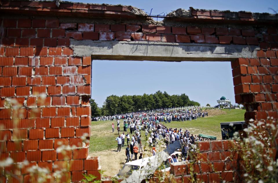 Bosnian Muslims carrying coffins of their relatives during a mass funeral are seen through a war-torn house in the village of Biscani, near Prijedor July 20, 2014. (REUTERS/Dado Ruvic)