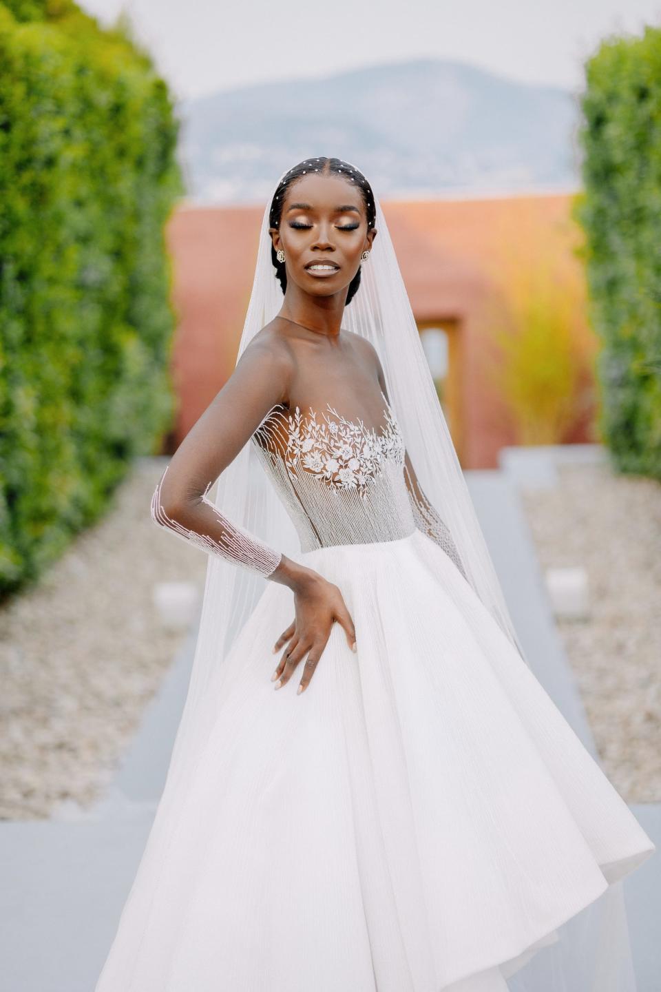 A bride puts a hand on her hip in front of a mountain.