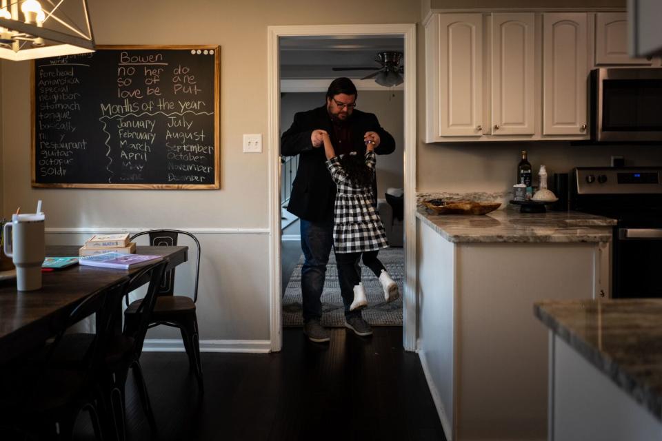 A man lifts his daughter by the hands in their home.